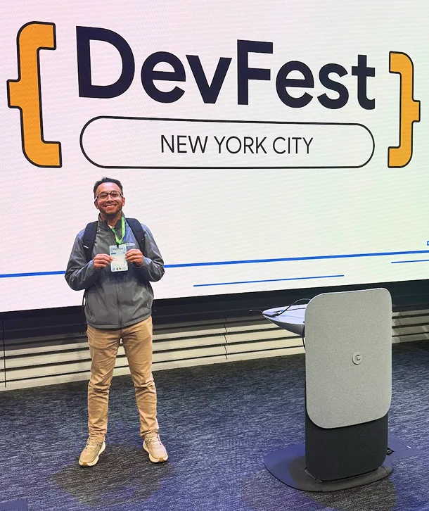 Ian Valeta smiling in front of a DevFest New York City backdrop, holding a name badge and wearing a lanyard.